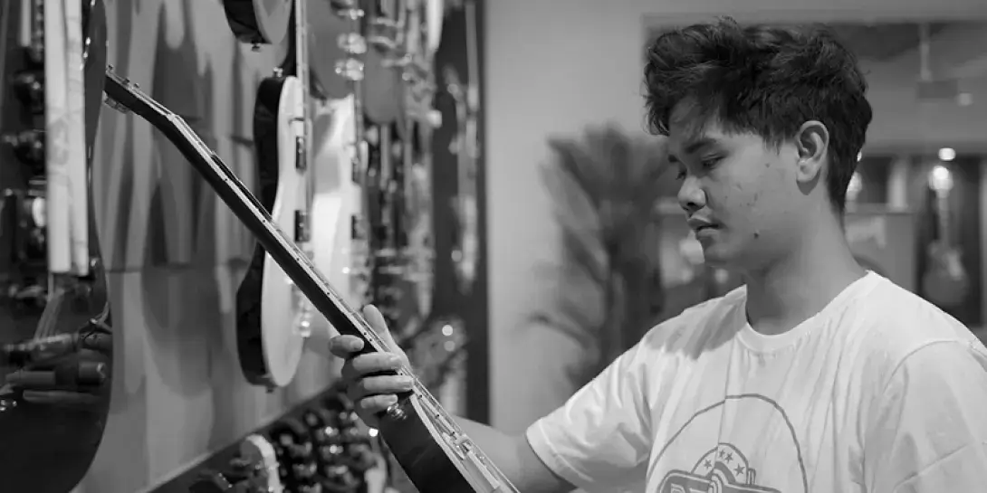 Denny Tawas holds an electric guitar in a music shop.