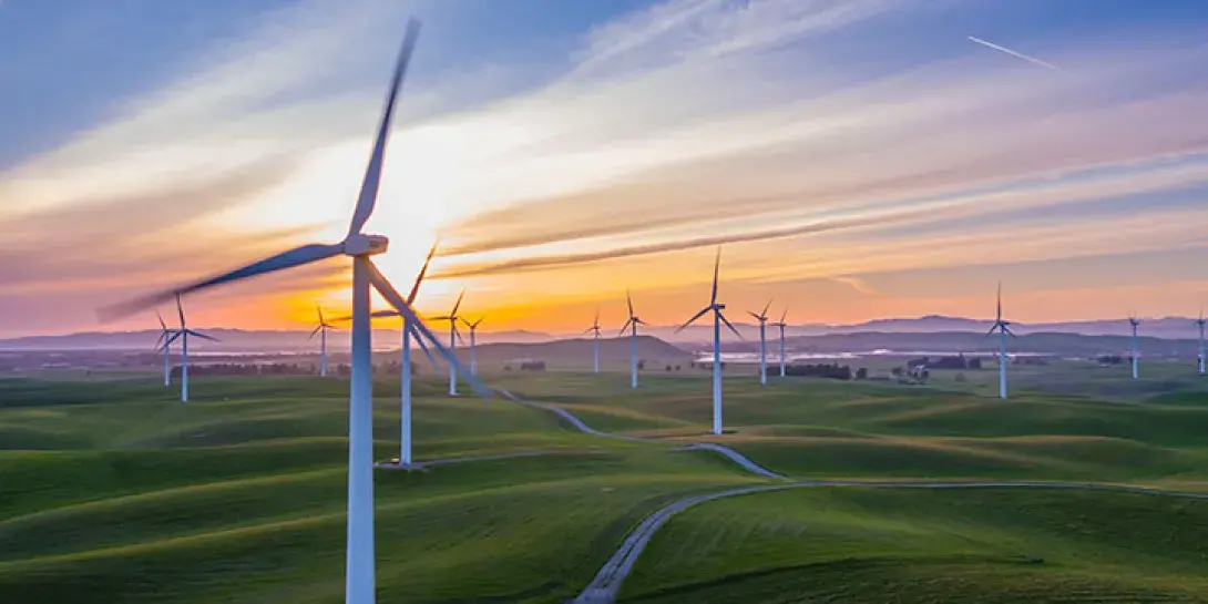 A wind farm set on some rolling hills at sunset