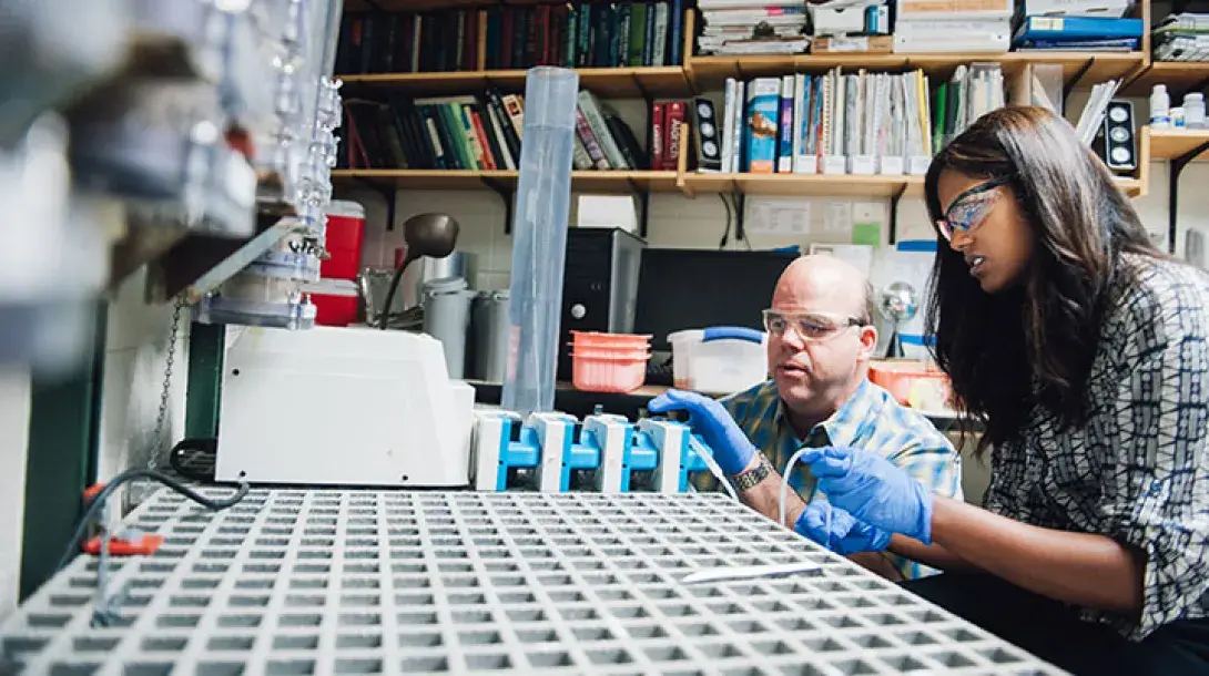 A professor and student sit side-by-side doing water-related research in a lab.