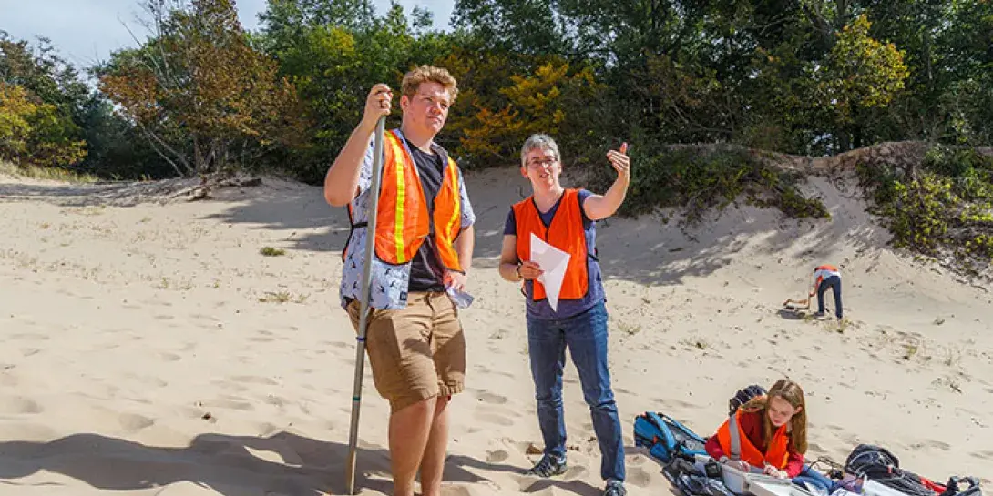 A professor and student wearing orange vests talking on a sand dune while doing field research.