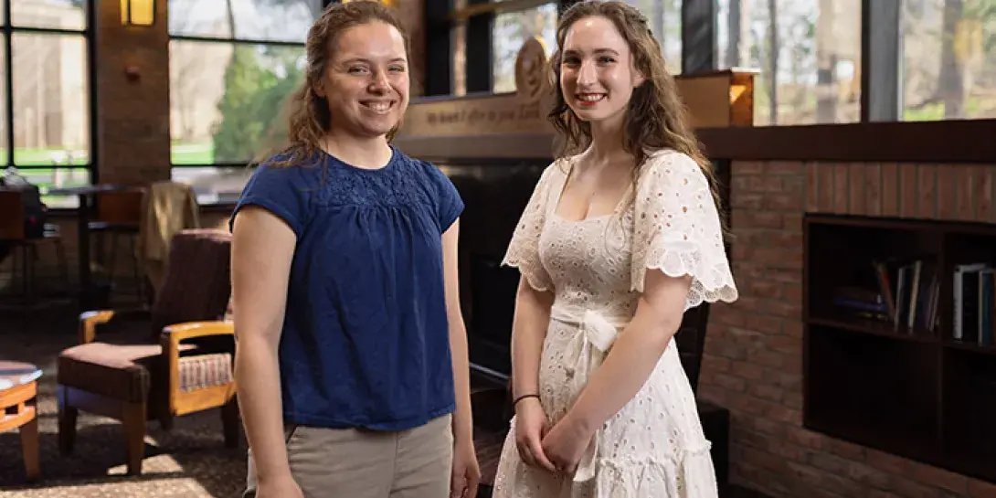 Graduating seniors Sarah Gibes and Michelle Merritt stand next to each other indoors.