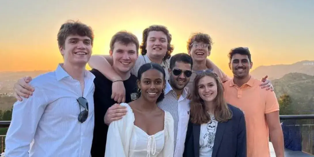 A group of eight students posing together at sunset with Hollywood sign and mountains in backdrop.