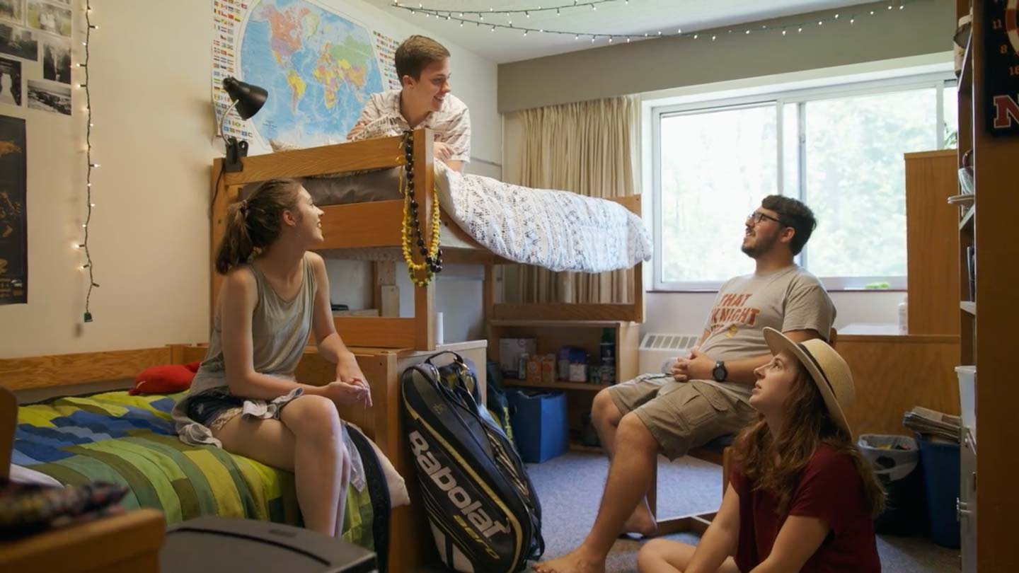 Four students (two male, two female) having a great conversation in a dorm room.