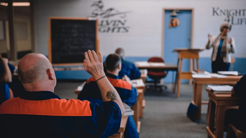 Inside prison classroom, inmate raising hand