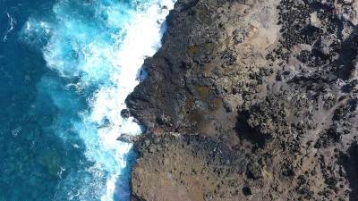 Overhead ocean scene featuring cerullean blue water and lava rock.