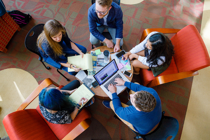 A group of students sit together with laptops.