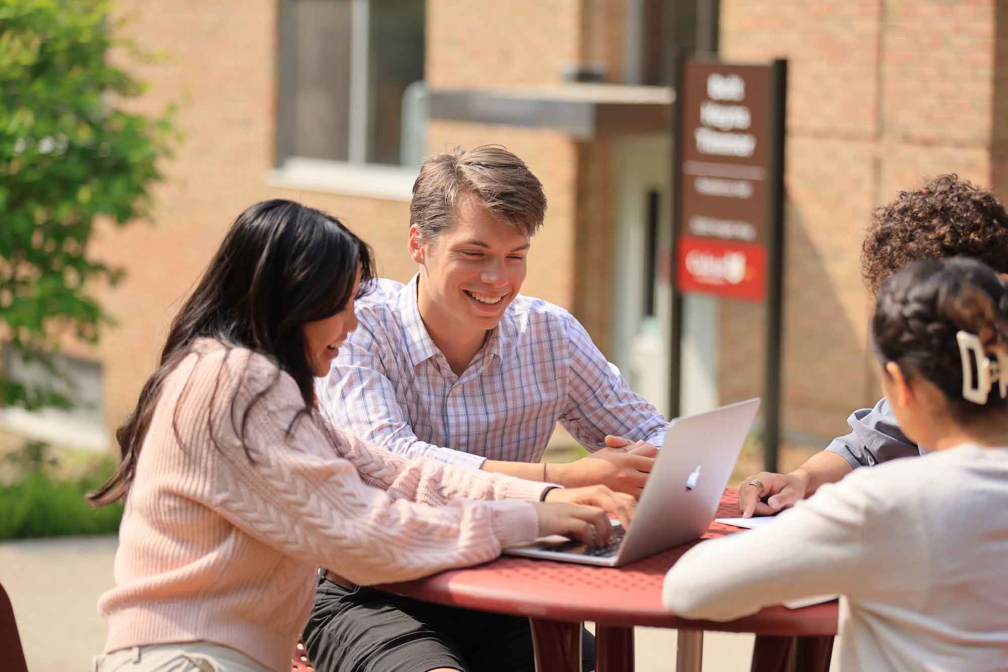 Students work on a computer outside at a table.