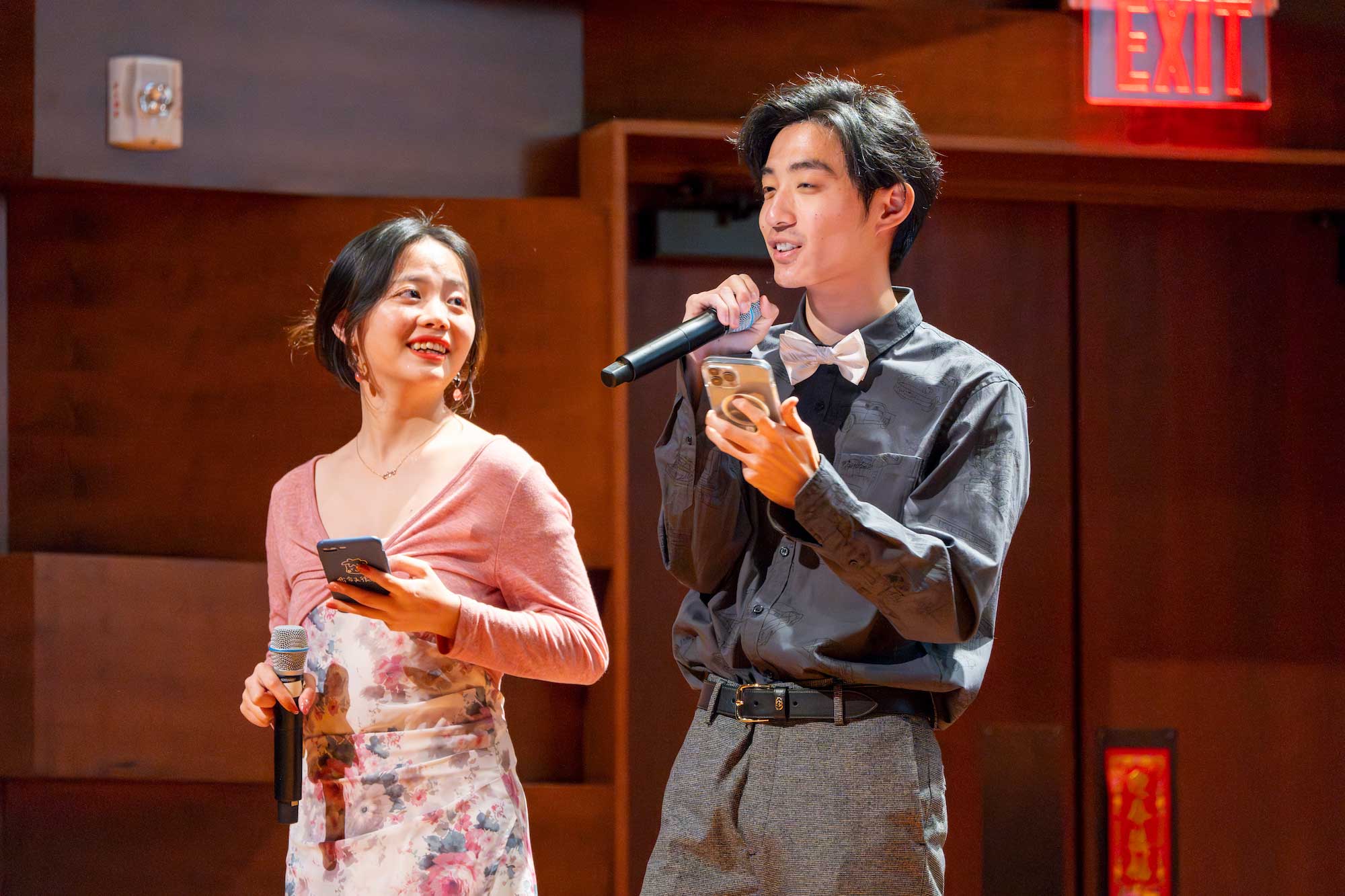 Two students talk into microphones on a stage.