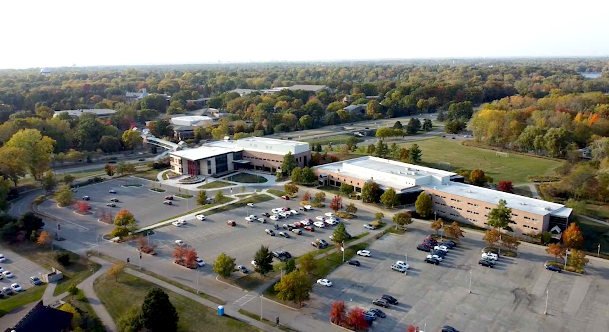A drone shot of the Prince Conference Center and Hotel, with a large parking lot, surrounded by trees, with the rest of the Calvin University campus in the background.