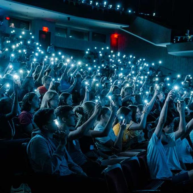 Calvin students in the darkened fine arts center holding up their phones with lights toward the stage