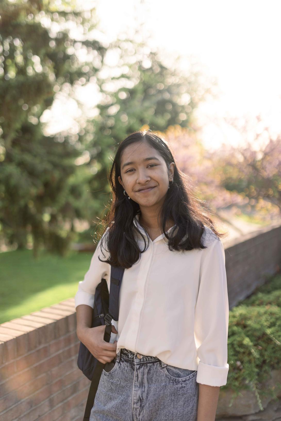 A student poses for the camera, smiling, with the sun shining behind.