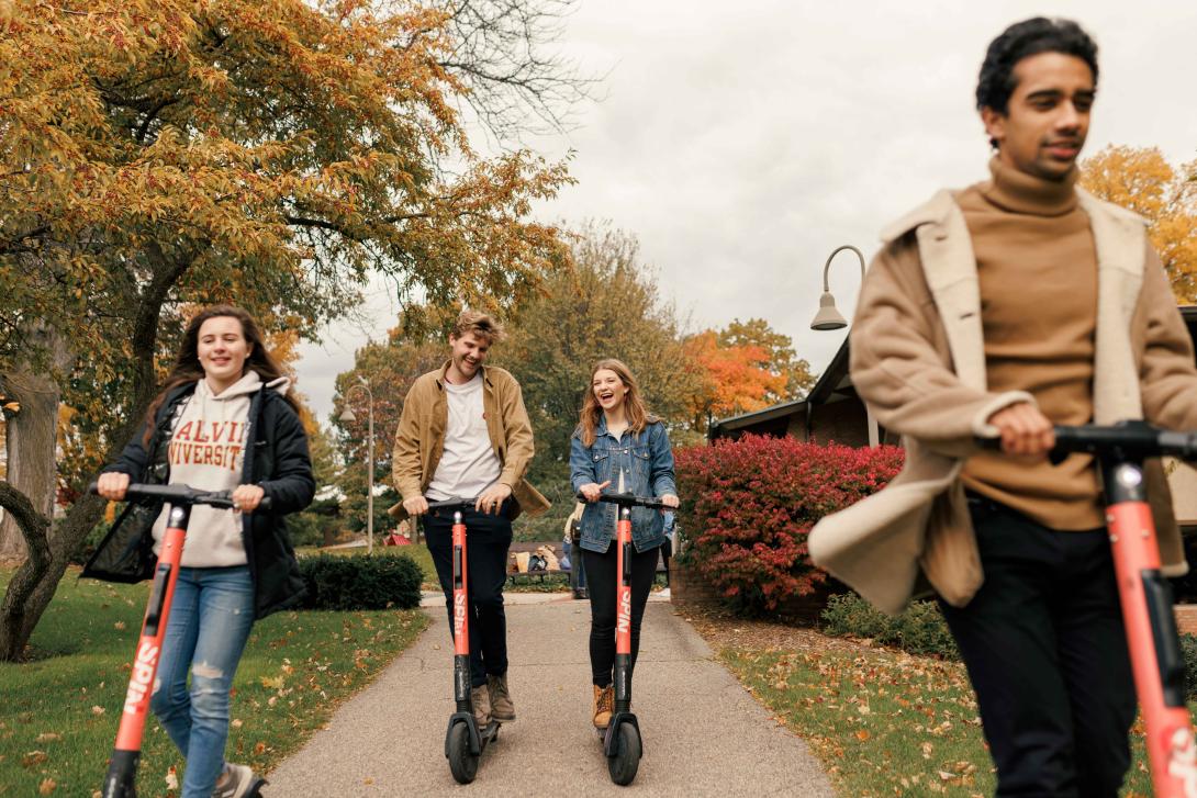 Four students ride electric scooters on Calvin University campus.