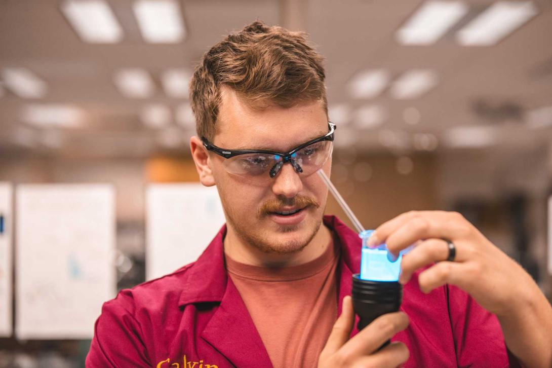 A student in a red lab coat with safety glasses on in the lab.