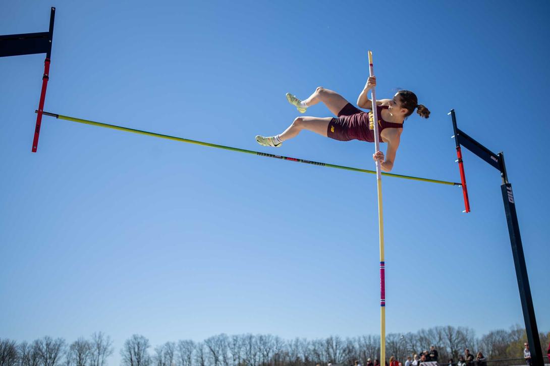A women's track and field athlete pole vaults over the bar.